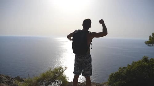 Man Celebrates Reaching Cliff Overlooking Ocean