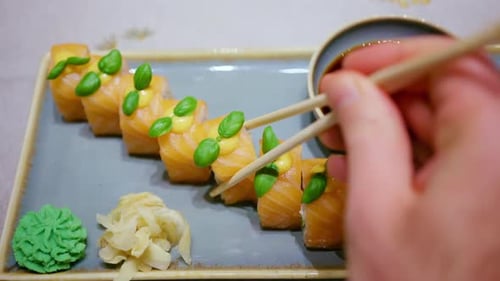 Chopsticks pick up a piece of sushi and dip it into soy sauce