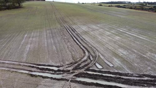 Aerial drone shot of a muddy farmers field with waterlogged tyre tracks.