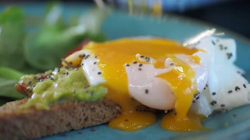 Cutting Open Poached Egg Over Avocado Toast
