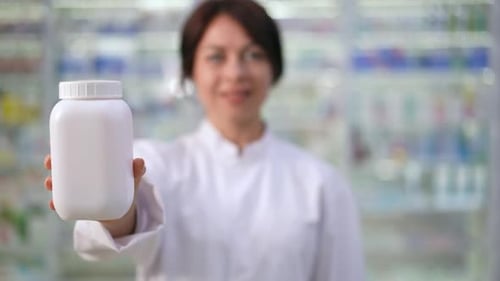 Closeup White Pill Bottle in Hand of Blurred Woman Standing in Pharmacy