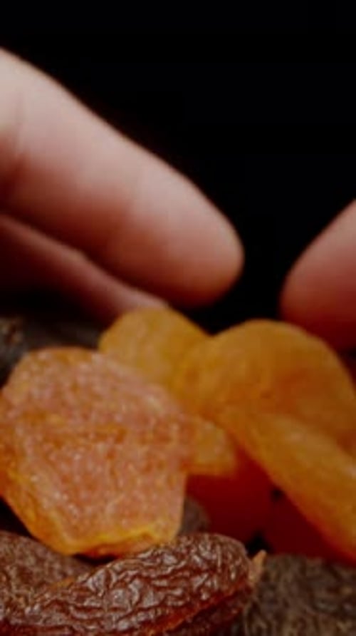 Vertical video. I Gather by Hand Two Types of Dried Apricots Against a Black Background. Dolly slide