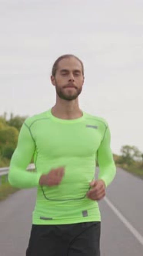 Smiling Runner Handsome Man in Green Bright Sportswear Running on the Country Road Outside Athletic