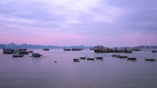 Vietnamese traditional fishing trawler boats float against karst mountains in Ha Long Bay at sunset