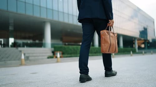 Nahaufnahme eines Geschäftsmannes, der mit den Beinen geht, während er eine Tasche hält. Ansicht von hinten. Jubelnd.