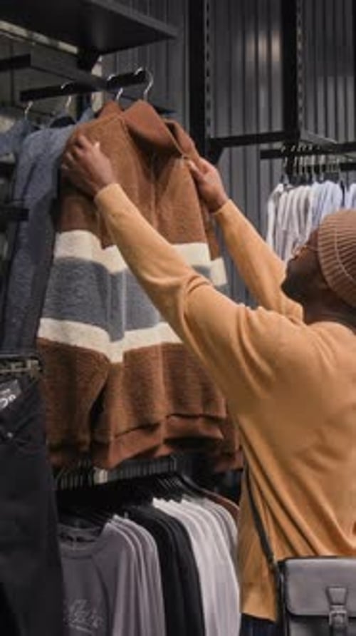 Vertical of Black Man Looking at Brown Sweater Jacket in Clothes Store