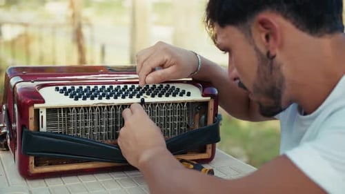 Man Repairs Accordion Outdoors in Daytime