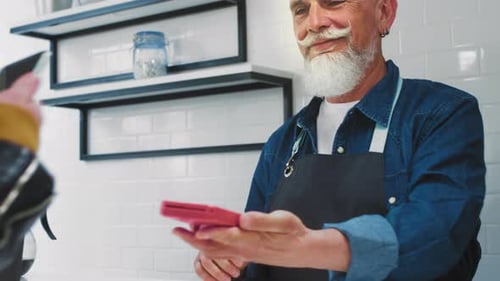 An Old Man in a Cafe Gives an Order to a Girl Client Senior Waiter or Barista Prepares Take Away
