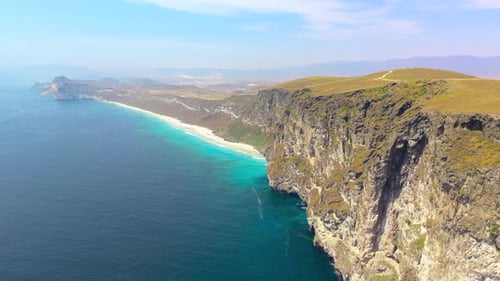 Aerial Perspective of Steep Rocky Cliffs Overlooking a Turquoise Sea and Sandy Beach Coastline Near