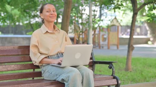 Young Woman in Park with Laptop Showing Approval Gesture