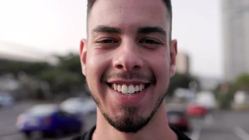 Outdoor portrait: happy young guy smiling at camera outdoor with city on background