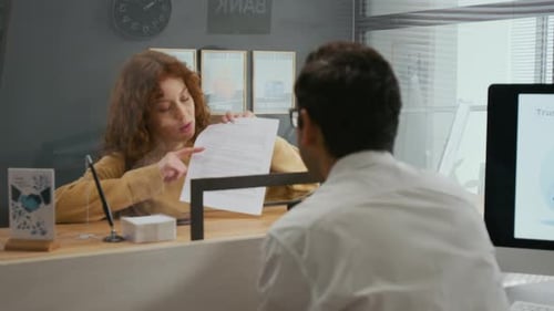 Woman Interacting with Bank Employee Across Glass Teller Window