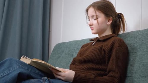 Focused Teenager Reading a Book on Couch