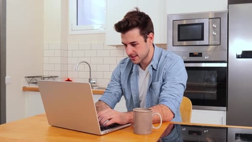 Handsome Caucasian Young Man Working Remotely From Home with a Laptop Looking at Camera Front View