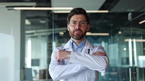 Smiling Male Doctor in Labcoat Posing with Crossed Arms in Modern Hospital
