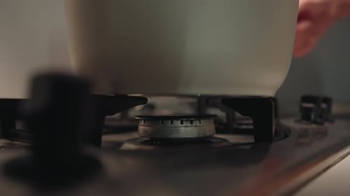 Man Placing Pot Onto Gas Stove and Turning Burner Preparing for Cooking Session in Dark Kitchen
