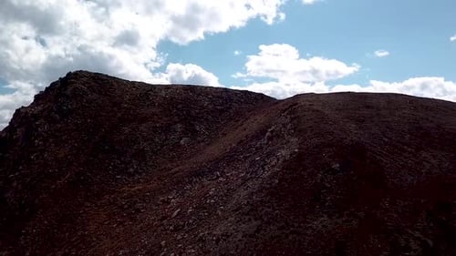 Drone shot flying past a mountain ridge revealing a beautiful valley and distant mountain range on a