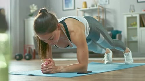 Starkes, schönes Fitness-Mädchen in athletischer Trainingskleidung macht eine Plankenübung, während sie ein S benutzt