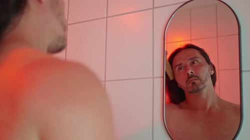 A Man Grooms Himself in Front of a Redlit Bathroom Mirror Creating a Captivating Ambiance