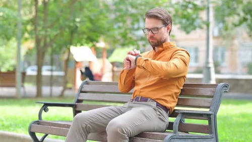 Man Checks Smartwatch While Sitting on Park Bench