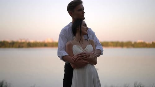 A Couple Embraces By the Tranquil Lake at Sunset Creating a Scene of Love and Elegance