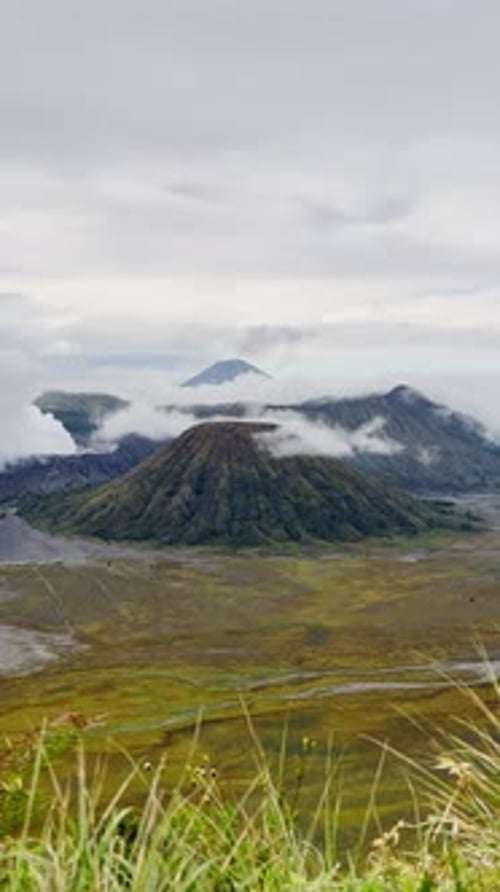 Imágenes verticales del cráter del monte Bromo con vapor que se eleva sobre la caldera y la sabana verde en Java Oriental