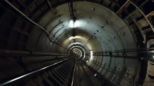 Geschwungener unterirdischer U-Bahn-Tunnel mit Stahlschienen und Betonsegmentverkleidung, beleuchtet von