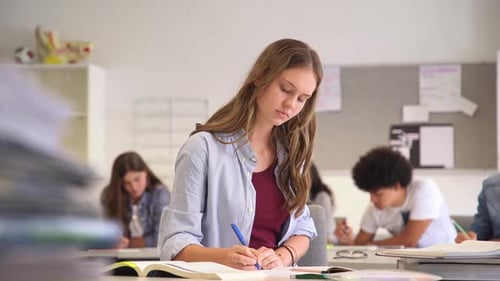 Portrait Of Smiling High School Student With Classmates In Background Writing Notes In The Classr...