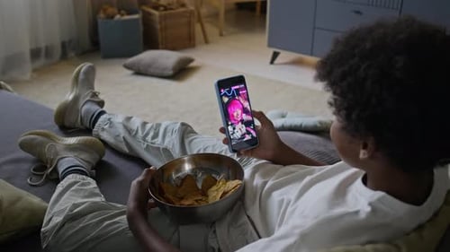 Schoolboy Enjoying Watching Live Stream on Phone with Bowl of Potato Chips
