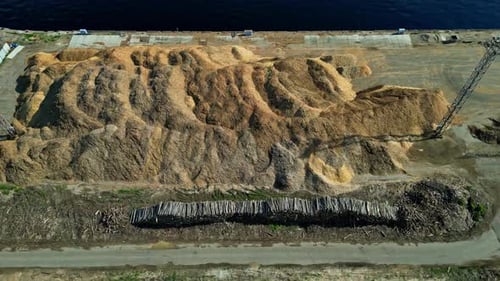 Tree trunks and large pile of wood fibers heaped up at the harbor, aerial slider