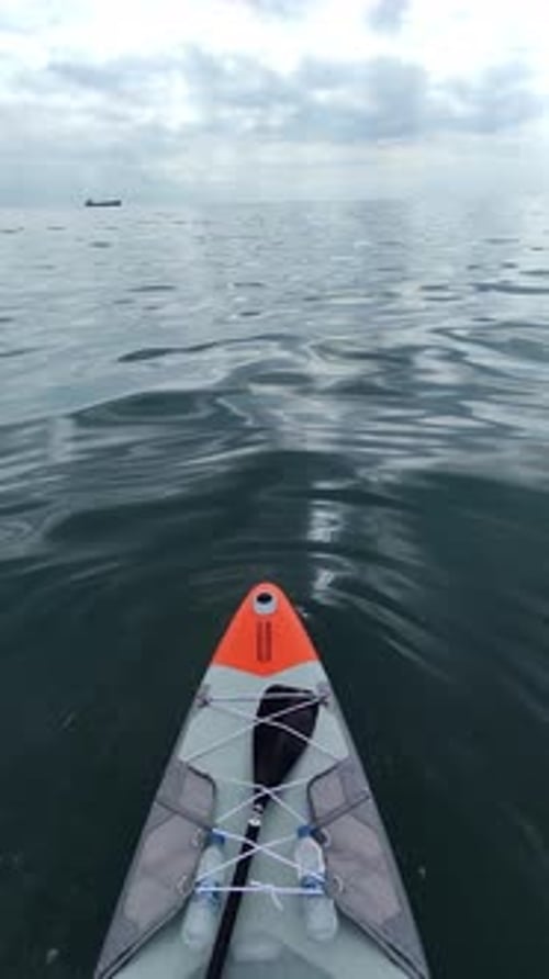 A Standup Paddleboard with Paddles and Water Bottles Floating on Calm Ocean Waters Under a Cloudy