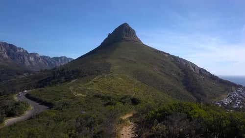 Cars drive up a windy road heading towards Lions Head Mountain Peak in Cape Town South Africa, Drone