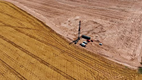 Oil rig with few cars and trucks around. Vast field and wheat plantation around the site.