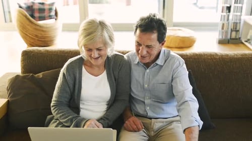 Senior Couple Laughing Using Laptop on Brown Sofa
