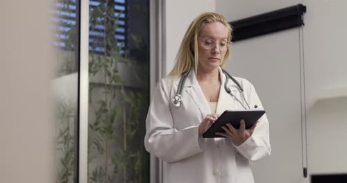 Female Doctor Holding Digital Tablet While Reviewing Patient Data in Hospital Office Setting with