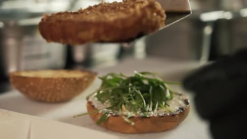 Close-up of chef hands wearing black glove adding burger on bread. Slow-motion