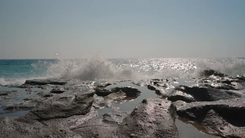 Waves Crashing on a Rocky Shoreline in Slow Motion. Sunlight Reflects Off the Water, Creating