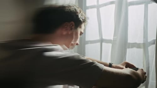 Jeune homme bouleversé assis près de la fenêtre dans une profonde apathie