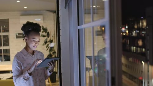 African American woman reviews data on a tablet at night in a business office