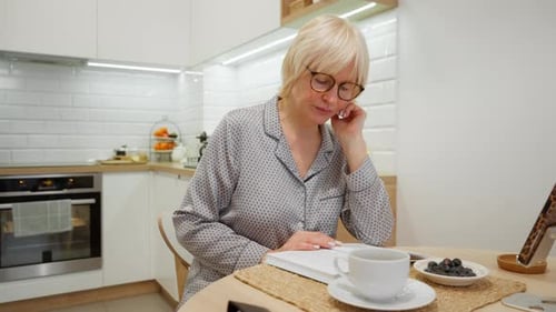 Elderly woman in pajamas reading a book during her quiet morning at home