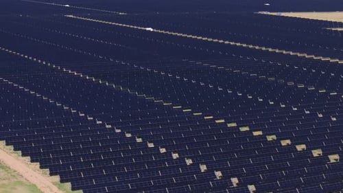 A large solar panel field in a sunny, rural landscape with clear skies, aerial view