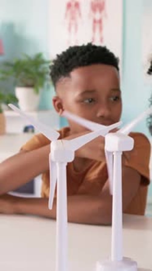Vertical video: Reaching youth in orange tee spinning and inspecting two turbines on table in study