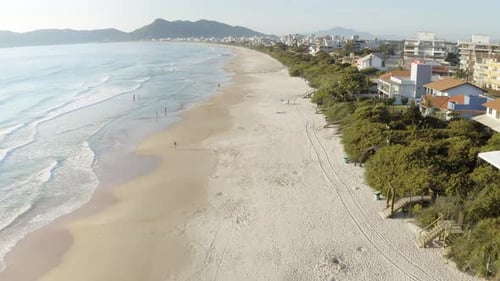 Drone flying over a beach with waves rolling in / Coastal landscape with mountains in the background