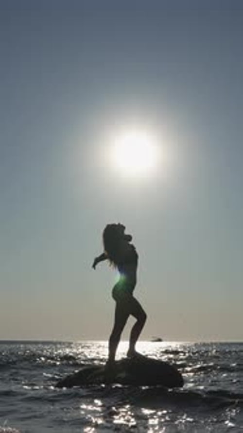 A Striking Silhouette of a Woman Gracefully Perched on a Rock Set Against the Backdrop of a Bright
