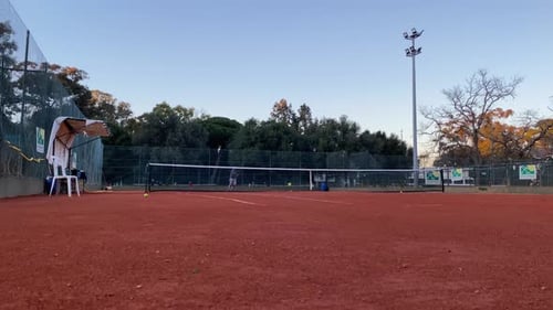 A couple demonstrates their tennis technique on a red ground court, with the woman executing a perfe