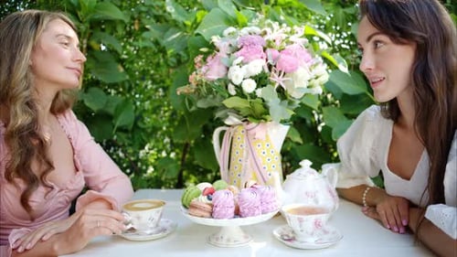 Frauen sprechen an einem Tabale mit einer Komposition aus Blumen, Makronen, Süßigkeiten, Nachtisch und Kaffee und Tee.