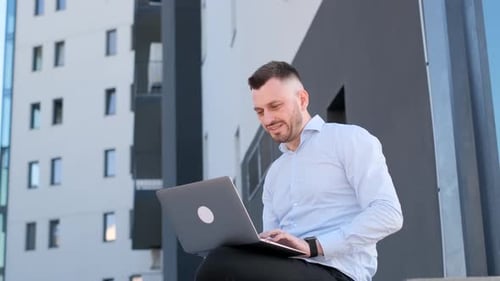 Young Businessman Working Online with a Laptop While Sitting on a Bench Outside of His Office