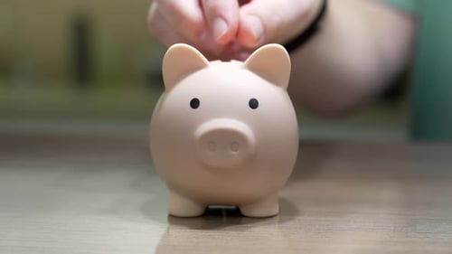 Hand depositing coins into piggy bank for retirement savings concept