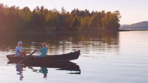 Stunning cinematic shot of a couple rowing on a swedish lake at sunset