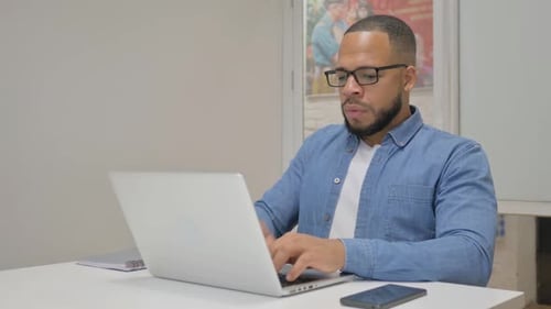 Coughing African Businessman Using Laptop in Office